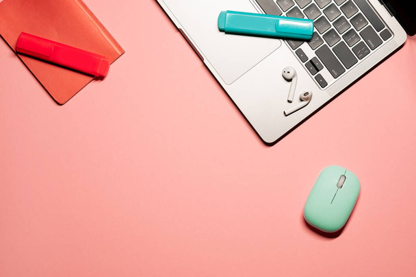 Composition plate et colorée avec un ordinateur portable moderne, une souris d'ordinateur sans fil, des marqueurs turquoise et corail, des écouteurs et un carnet sur fond rose. - Photo, image