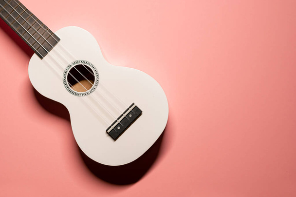 Minimalist düz çekim, beyaz ukulele Hawai gitarı ve pastel pembe arka planda naylon teller.. - Fotoğraf, Görsel