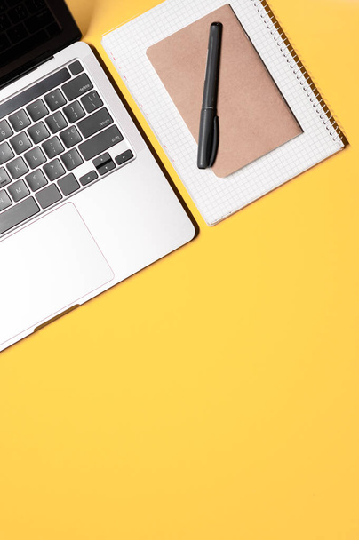 Vertikales Layout mit einem silbergrauen modernen Laptop, zwei einfachen Notizbüchern, grauem Liner und einem Kopierraum auf gelbem Hintergrund. - Foto, Bild