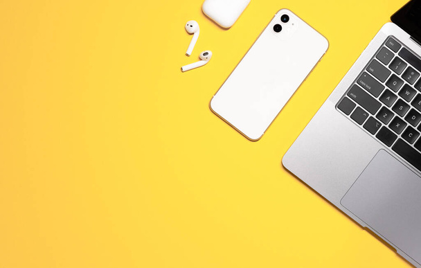 Plan plat coloré d'un ordinateur portable gris argenté, smartphone blanc, écouteurs avec un étui de charge sur un fond jaune. - Photo, image
