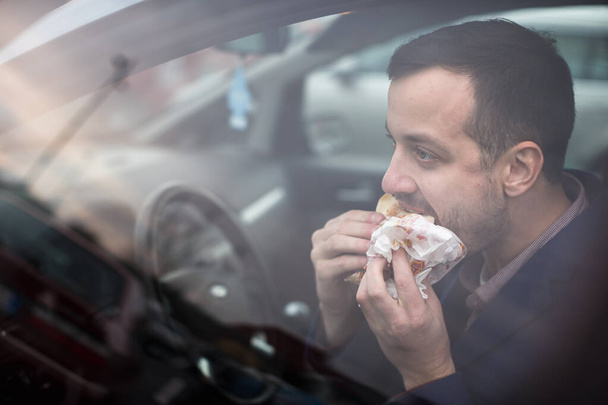 Handsome young man eating a hurried lunch in his car (color toned image; shallow DOF) - Foto, immagini