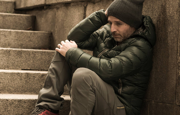 σκοτεινό και ευερέθιστο αστικό πορτρέτο του μεσήλικα θλιμμένου και καταθλιπτικού άνεργου άνδρα που κάθεται σε εξωτερικούς χώρους στις βρώμικες σκάλες της γωνίας του δρόμου και αισθάνεται αναστατωμένος που υποφέρει από κατάθλιψη - Φωτογραφία, εικόνα