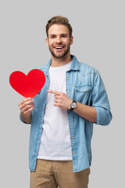Portrait of charming man hold hand paper heart shaped card wear casual style shirt isolated over grey background - Foto, imagen