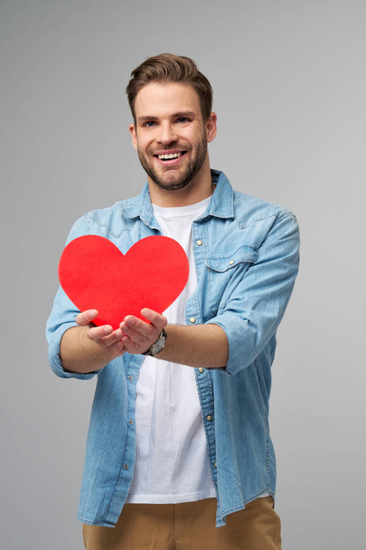 Portrait of charming man hold hand paper heart shaped card wear casual style shirt isolated over grey background - Fotoğraf, Görsel