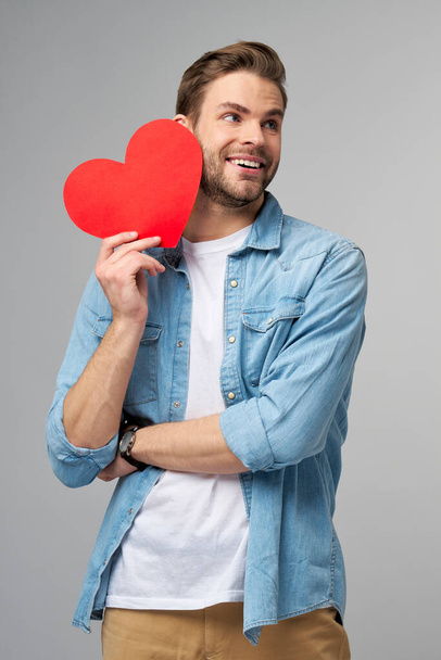 Portrait of charming man hold hand paper heart shaped card wear casual style shirt isolated over grey background - Foto, afbeelding