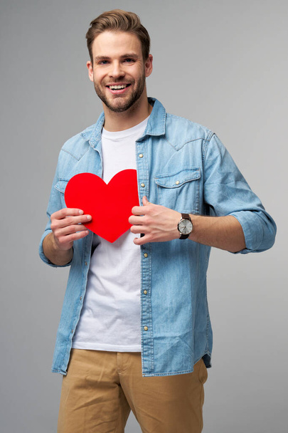 Portrait of charming man hold hand paper heart shaped card wear casual style shirt isolated over grey background - Fotografie, Obrázek