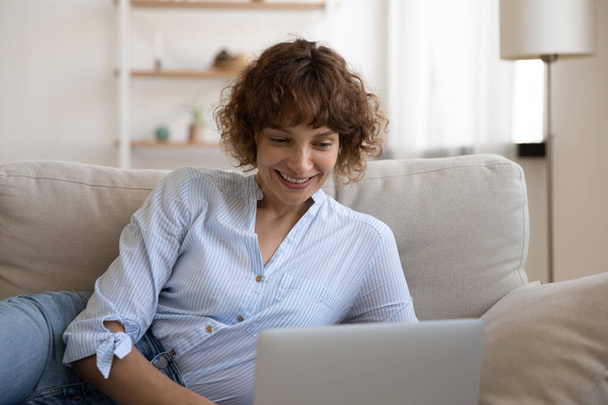 Confident lady recline on couch engaged in chatting by laptop - Foto, afbeelding