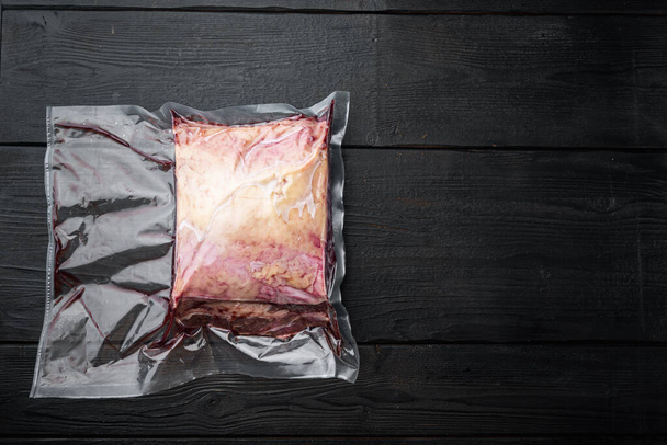Süpürge paketinde kesilmiş mermer çiğ biftek, siyah ahşap masa, üst görünüm, metin için kopyalama alanı ile - Fotoğraf, Görsel