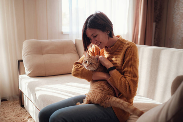 Young asian woman resting with pet in sofa at home in sunny. Beautiful ginger tabby cat. Animals and lifestyle concept. - Fotografie, Obrázek