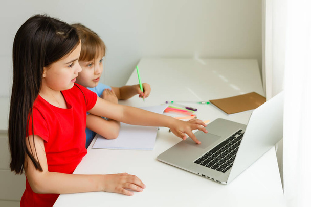 Két lányt, a legidősebbet és a legfiatalabbat, eljegyeztek egy asztalnál egy laptopon.. - Fotó, kép