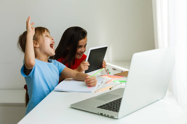 Ωραίο online σχολείο. Τα παιδιά μελετούν διαδικτυακά στο σπίτι χρησιμοποιώντας ένα λάπτοπ. Χαρούμενα νεαρά κοριτσάκια που χρησιμοποιούν φορητό υπολογιστή μελετώντας μέσω του online συστήματος ηλεκτρονικής μάθησης. Απόσταση ή εξ αποστάσεως μάθηση - Φωτογραφία, εικόνα
