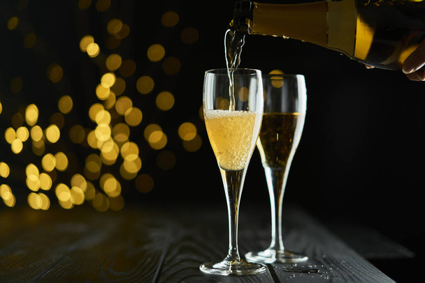 Два бокала игристого вина или шампанского в ознаменование Нового года, Рождества или Юбилея с боке-эффектом. Желтый цвет вина и огней выделяется на темном фоне. - Фото, изображение