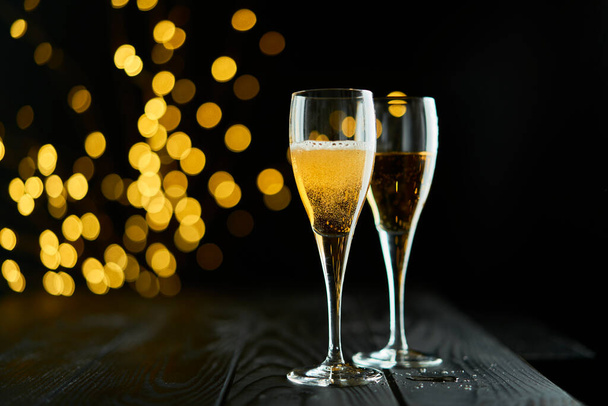 Twee glazen mousserende wijn of champagne om nieuwjaar, vrolijk kerstfeest of jubileum met een bokeh effect achtergrond te vieren. Het geel van de wijn en de lichten vallen op tegen een donkere achtergrond. - Foto, afbeelding