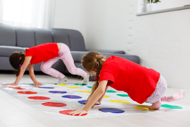 Two happy girls in children's clothes enthusiastically play on the floor. - Fotoğraf, Görsel