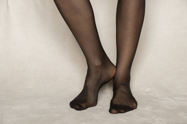 vrouwelijke benen in zwart nylon panty op een wit tapijt thuis - Foto, afbeelding