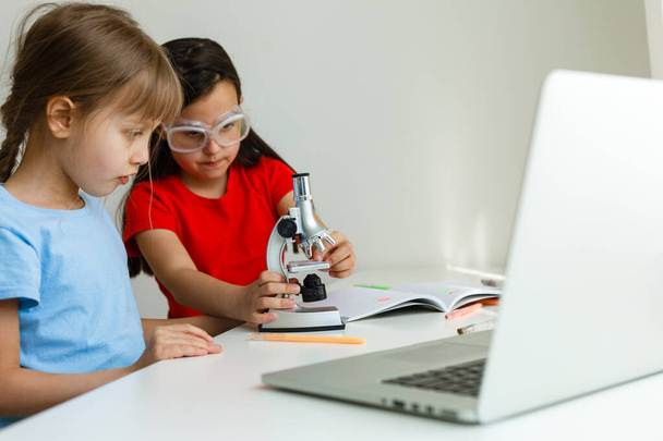 Fajna szkoła online. Dzieci uczą się online w domu za pomocą laptopa. Wesołe małe dziewczynki korzystające z laptopa, które uczą się przez internetowy system e-learningowy. Odległość lub uczenie się na odległość - Zdjęcie, obraz