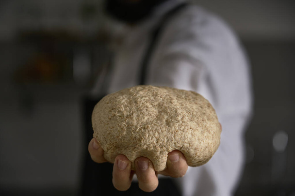 La main d'un homme cuisinier montre la pâte complète fraîchement pétri pour la cuisson du pain, pâtes, gâteau ou pizza. Dans sa cuisine, il perpétue la tradition des pâtes maison. - Photo, image