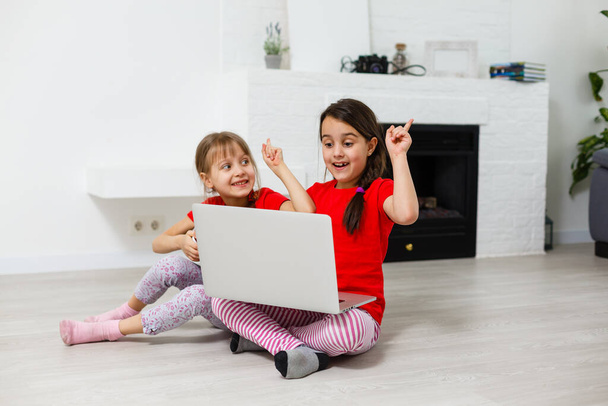 2人の小さな女の子がノートパソコンの前に座って笑い、クローズアップ、肯定的な感情、子供のためのインターネット上のエンターテイメント - 写真・画像