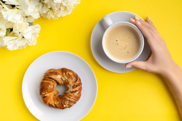 黄色の背景にコーヒーのカップを保持管理された女性の手。フラットレイ、トップビュー春の夏の朝食立ち上げブランチコンセプト. - 写真・画像