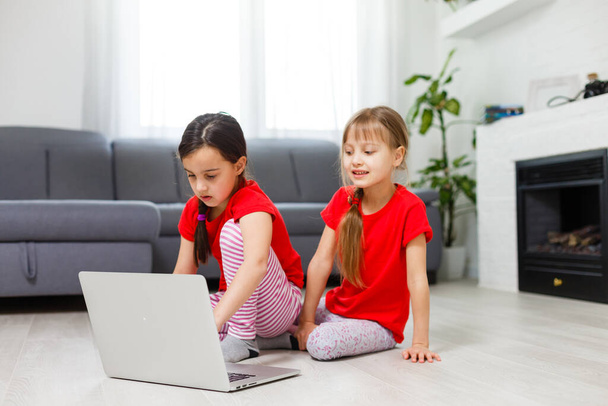 Két kislány ül egy laptop előtt és nevet, közelkép, pozitív érzelmek, szórakozás az interneten gyerekeknek - Fotó, kép