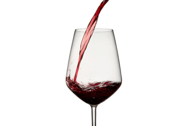 Stillleben-Fotografie auf weißem Hintergrund eines klaren Glasbechers mit Rotwein. Der Wein erzeugt Wellen, Tropfen und Blasen im Glas und ist bereit, jedes Ereignis zu feiern. - Foto, Bild