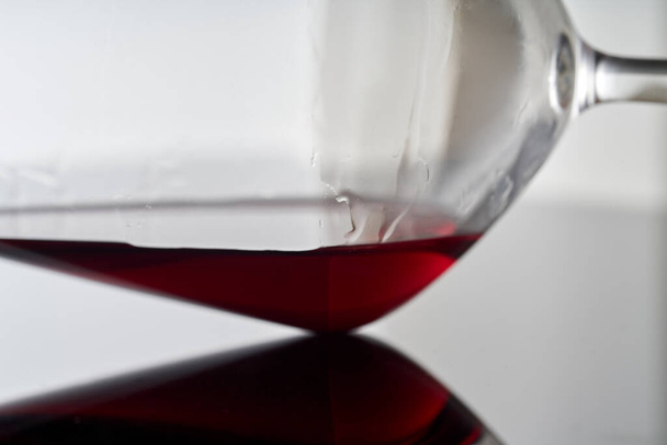 Zátiší fotografie sklenice s červeným vínem. Průhledný skleněný pohár na bílém pozadí leží na černém skleněném povrchu odrážejícím víno. - Fotografie, Obrázek
