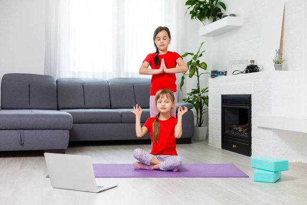 Две маленькие девочки практикуют йогу, растяжку, фитнес по видео на блокноте. Дистанционное онлайн обучение, аэробика дома. Здоровый образ жизни, коронавирус, оставайтесь дома. Карантин для детей. - Фото, изображение