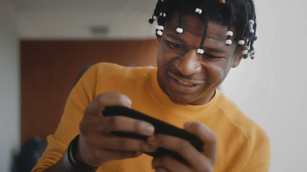 Πορτρέτο του εστιασμένου αφροαμερικανού μαύρου άνδρα που παίζει παιχνίδια στο smartphone  - Φωτογραφία, εικόνα