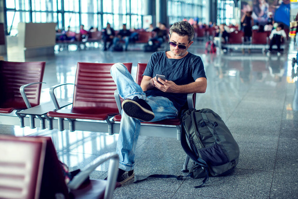 Joven revisando su teléfono mientras espera su vuelo en el aeropuerto en el área de salida - Foto, Imagen