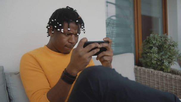 Retrato del hombre negro afroamericano enfocado jugando juegos en el teléfono inteligente  - Foto, Imagen