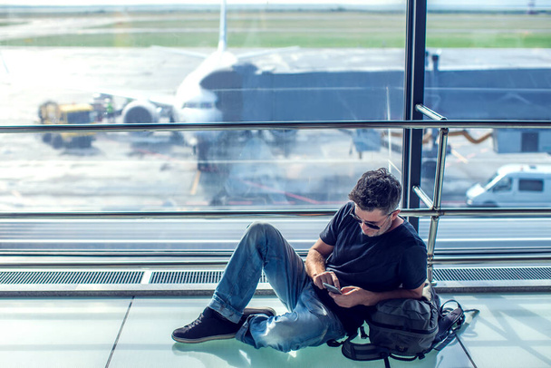 Fiatalember ellenőrzi a telefonját, miközben a repülőtéren várja a gépét. Utazási koncepció - Fotó, kép