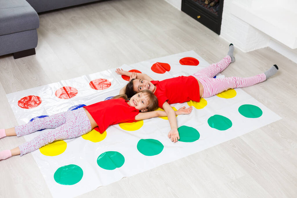 Dos niñas felices en ropa de niños juegan con entusiasmo en el suelo. - Foto, imagen