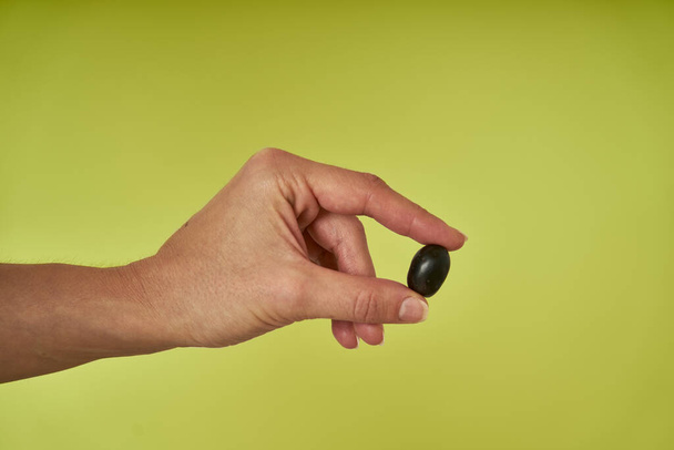 рука показывает черные оливки на зеленом фоне                      - Фото, изображение