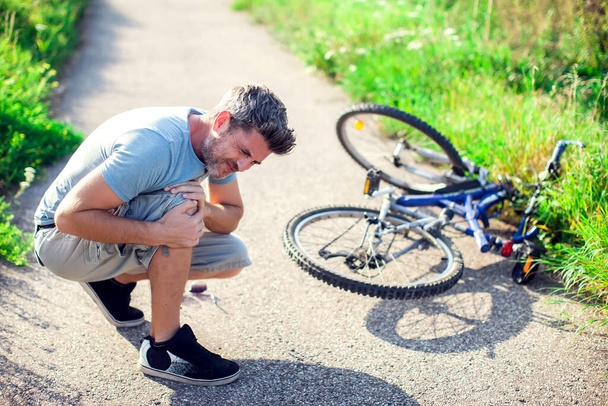 Man with dark hair with pain in knee joints after biking on bicycle. Sport, healthcare and people concept - Photo, Image