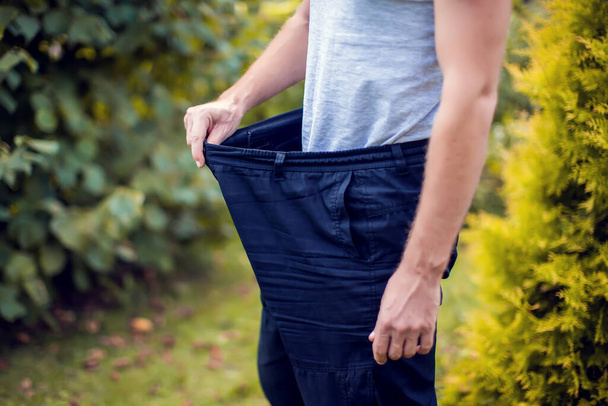 Junger Mann trägt große lockere Jeans im Freien - Konzept zur Gewichtsabnahme - Foto, Bild