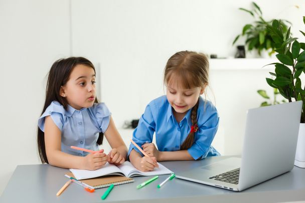Крутая онлайн школа. Дети учатся дома с помощью ноутбука. Веселые маленькие девочки используют ноутбук, изучая систему электронного обучения онлайн. Дистанционное или дистанционное обучение - Фото, изображение