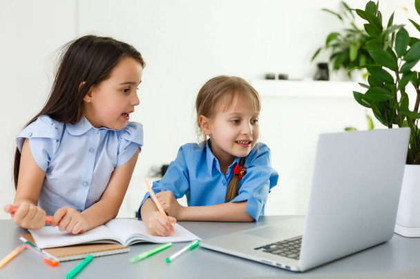 Cool escuela en línea. Los niños que estudian en línea en casa usando un ordenador portátil. Niñas alegres utilizando ordenador portátil estudiando a través del sistema de e-learning en línea. Enseñanza a distancia o remota - Foto, Imagen