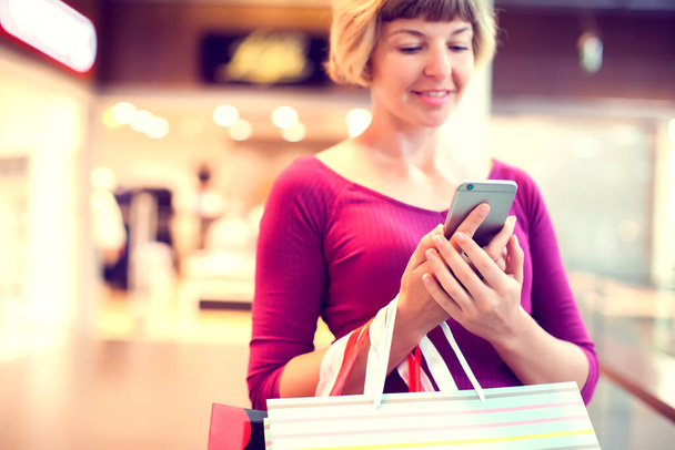 Γυναίκα πελάτης με κινητό τηλέφωνο και τσάντες για ψώνια στο εμπορικό κέντρο - Φωτογραφία, εικόνα