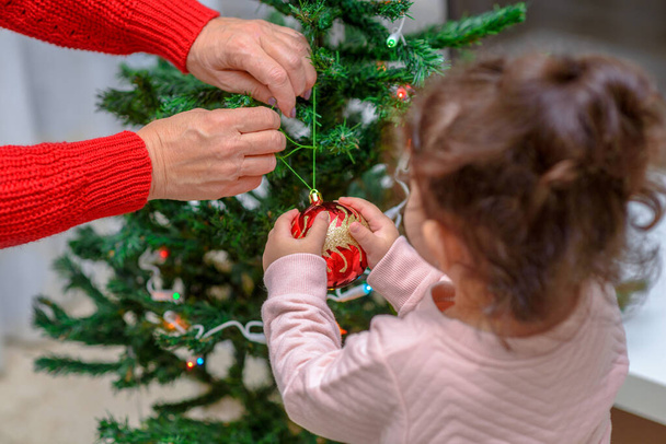 Grandmother and grandchild decorate the Christmas tree with baubles indoors. Portrait loving family close up. - Foto, Imagen