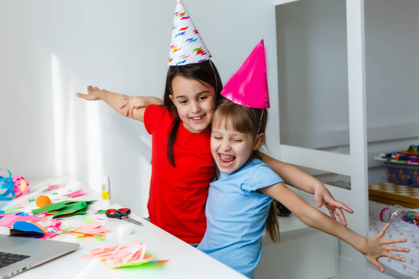 Kids online birthday party. Little girls in dresses, hat celebrate holiday with friends. Conference,video call in laptop, computer. Quarantine, coronavirus pandemic covid-19. - Photo, Image
