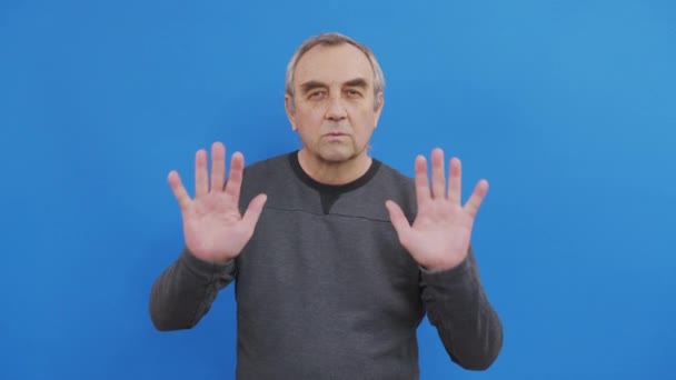 Dissatisfied elderly gray-haired mustache man in casual t-shirt isolated on bright blue color background studio. People lifestyle concept. Showing stop gesture with palm hands. - Footage, Video