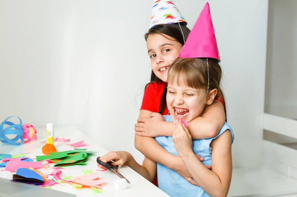 A little girl, curves and laughs in front of a laptop in a cap. Celebrates birthday via internet in quarantine time, self-isolation and family values, online birthday. Congratulations to the animator - Photo, Image