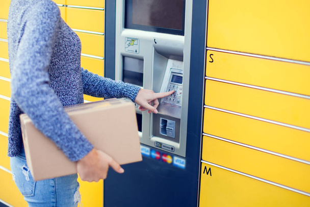Woman client using automated self service post terminal machine or locker to deposit the parcel for storage, - Photo, Image