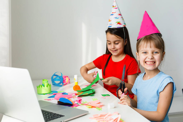 Kids online birthday party. Little girls in dresses, hat celebrate holiday with friends. Conference,video call in laptop, computer. Quarantine, coronavirus pandemic covid-19. - Photo, Image
