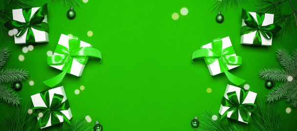 Зимовий фон зелений. Білі подарунки зі смарагдовим кольоровим бантом, зеленими кульками та блискучими вогнями в різдвяній прикрасі на зеленому фоні для вітальної листівки. Зимова святкова композиція з копією простору
 - Фото, зображення