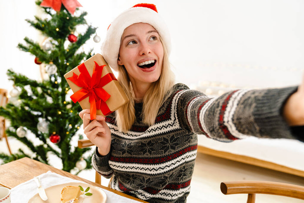 Happy nice girl taking selfie photo with present while having Christmas lunch at home - Φωτογραφία, εικόνα