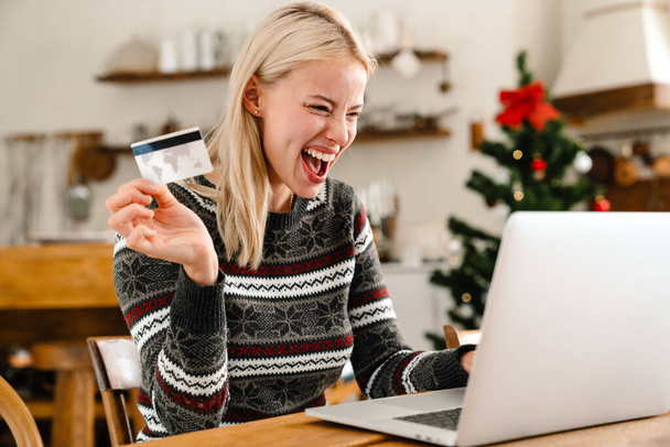 Image of a young excited surprised woman indoors at home using laptop computer and holding credit card - Фото, зображення