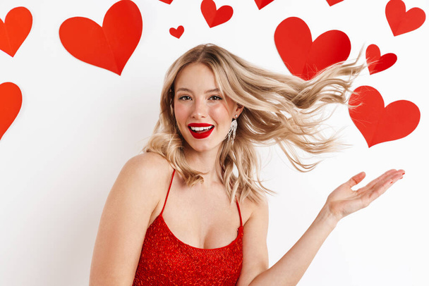 Photo of a young happy cheery blonde woman in red dress isolated over white background with hearts - Φωτογραφία, εικόνα