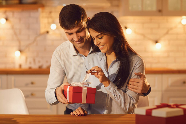 Young happy brunette woman unpacking holiday present from her smiling boyfriend - Foto, imagen