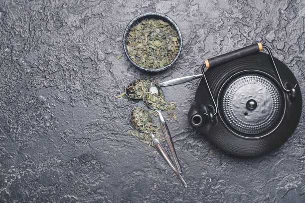 Teapot, bowl and spoons with dry green tea on dark background - Foto, immagini